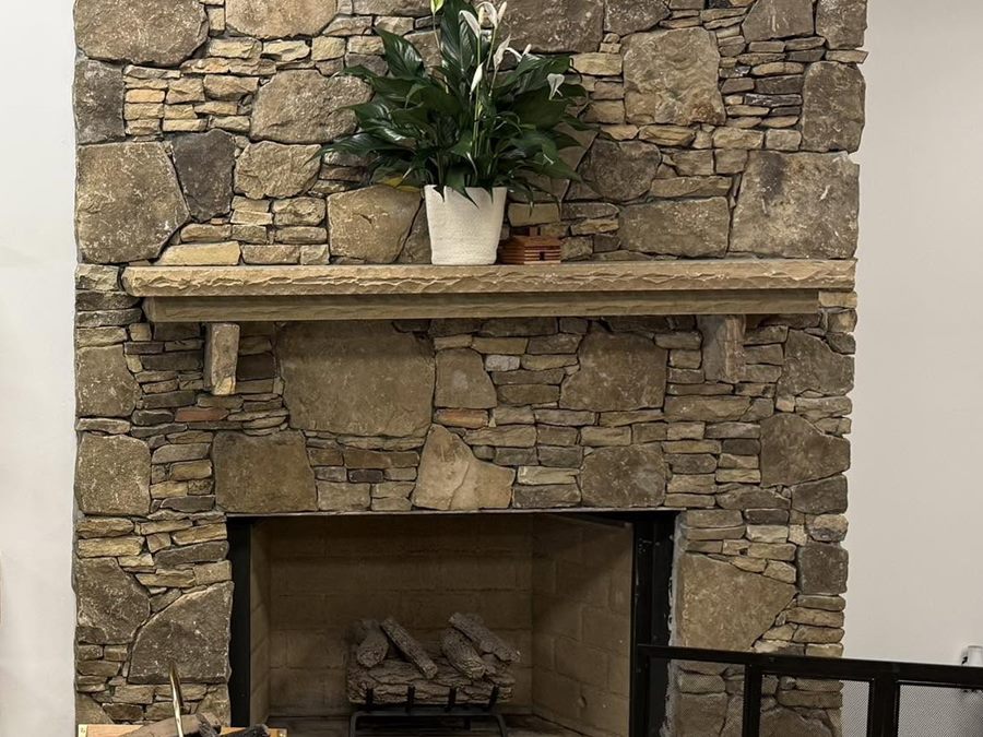 A stacked-stone fireplace with a rough-cut timber mantel in the Hearth Enterprises showroom