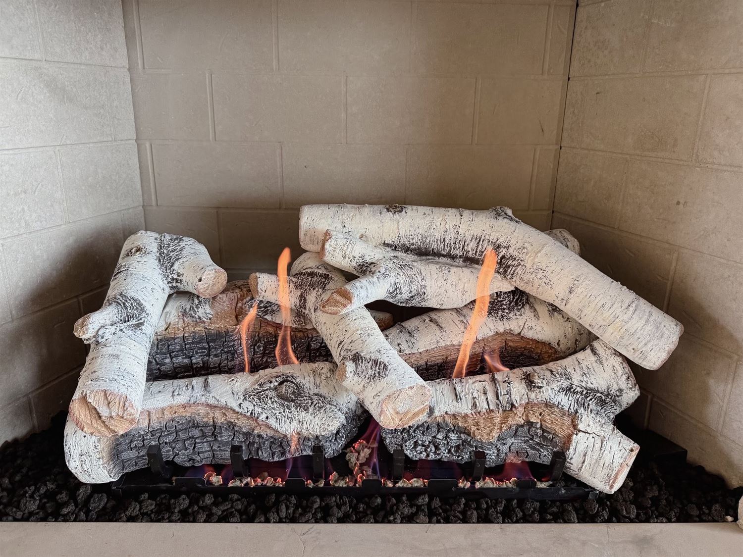 A white birch gas log set burning in a showroom fireplace at Hearth Enterprises