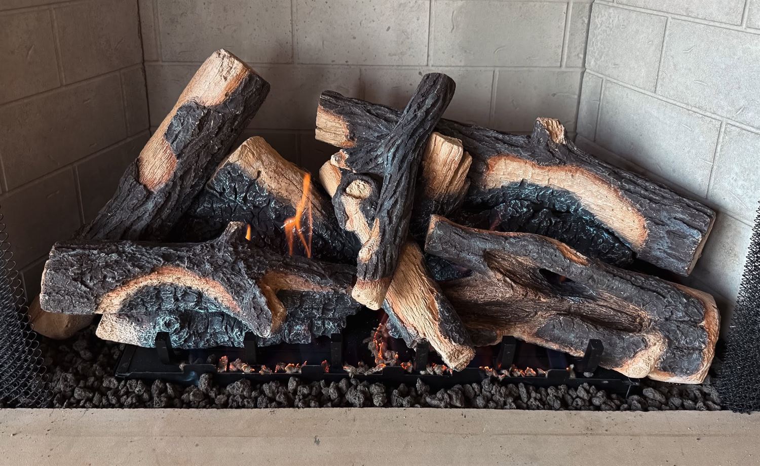 An oak-style gas log set burning in a showroom fireplace at Hearth Enterprises