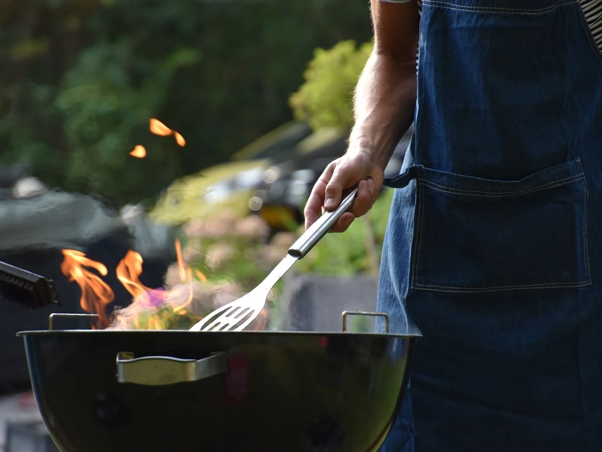 A person turning food on a lit kettle grill in a backyard