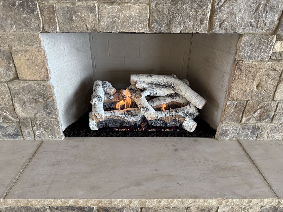 A white birch gas log set burning in a light stone fireplace