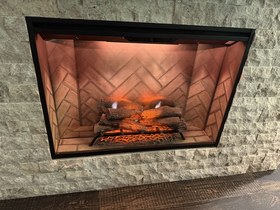 A gas fireplace insert with a herringbone firebrick interior, lit, set into a stone surround