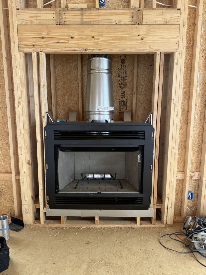 A fireplace box in stud framing with a metal flue pipe rising from the top into the chase above