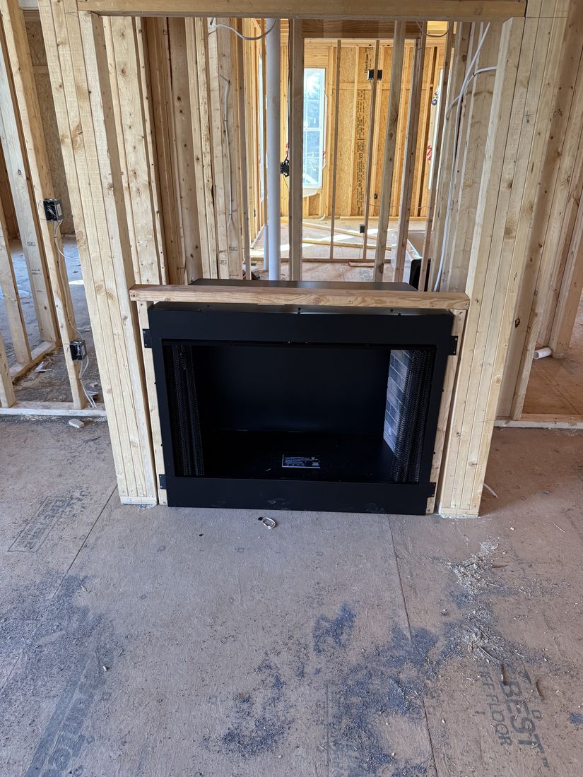 A black fireplace box set into bare stud framing on a concrete slab during construction