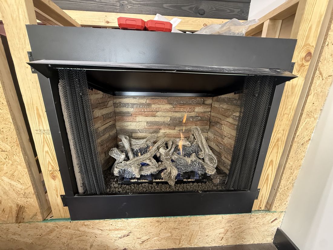 A gas fireplace burning inside a framed opening with bare studs still visible around it