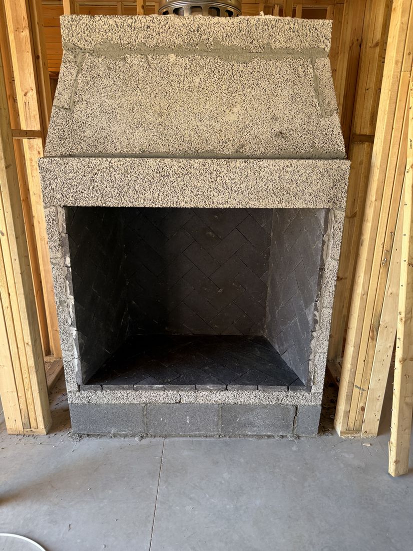 A masonry firebox with herringbone firebrick and a concrete throat, framed into a wall under construction