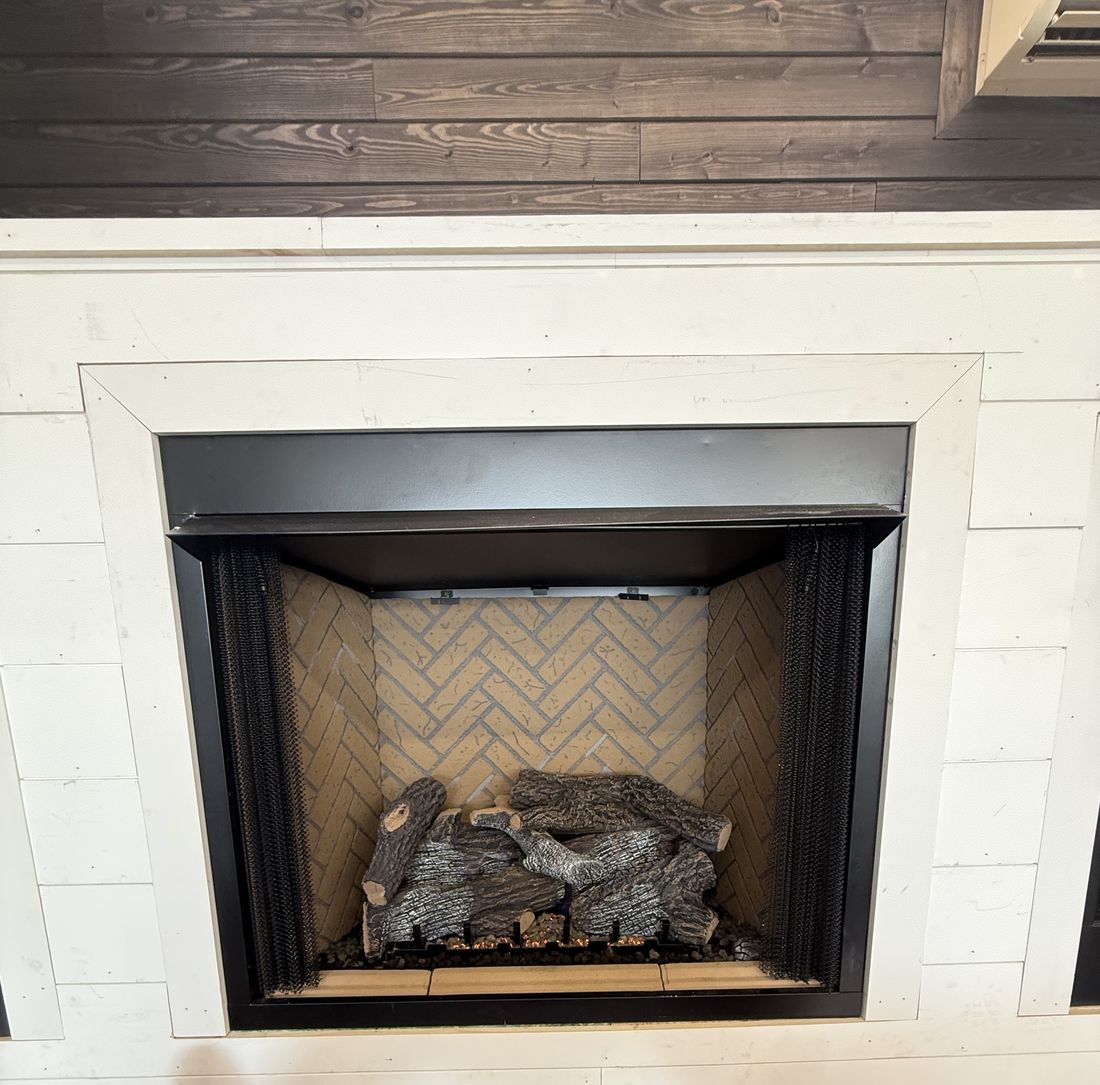 A white shiplap fireplace surround with a black firebox and herringbone firebrick behind an unlit gas log set