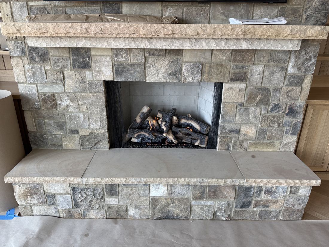 A stone fireplace with a cast stone mantel shelf and a gas log set, hearth still covered during construction