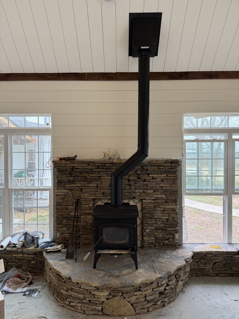 The same wood stove installation seen wider, with the black stovepipe running up to a ceiling support box